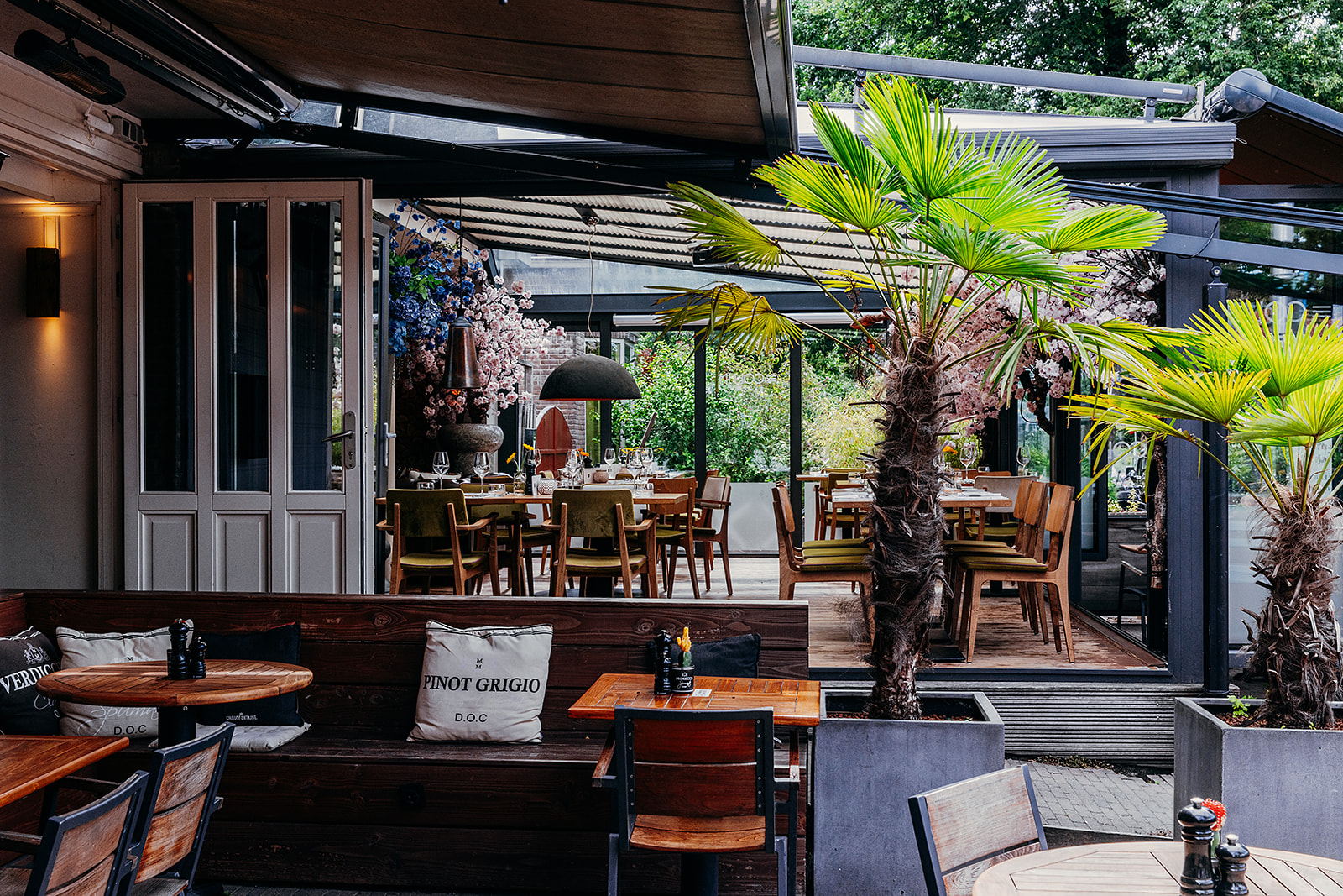 Het terras van Restaurant Colijn, overdekt met groene palmen en sfeervol gedekte tafels